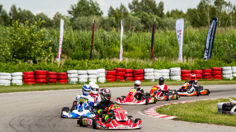 Kartingai vaikams: vaikai su šalmais lenktyniauja sportiniais kartingais lauko trasoje.